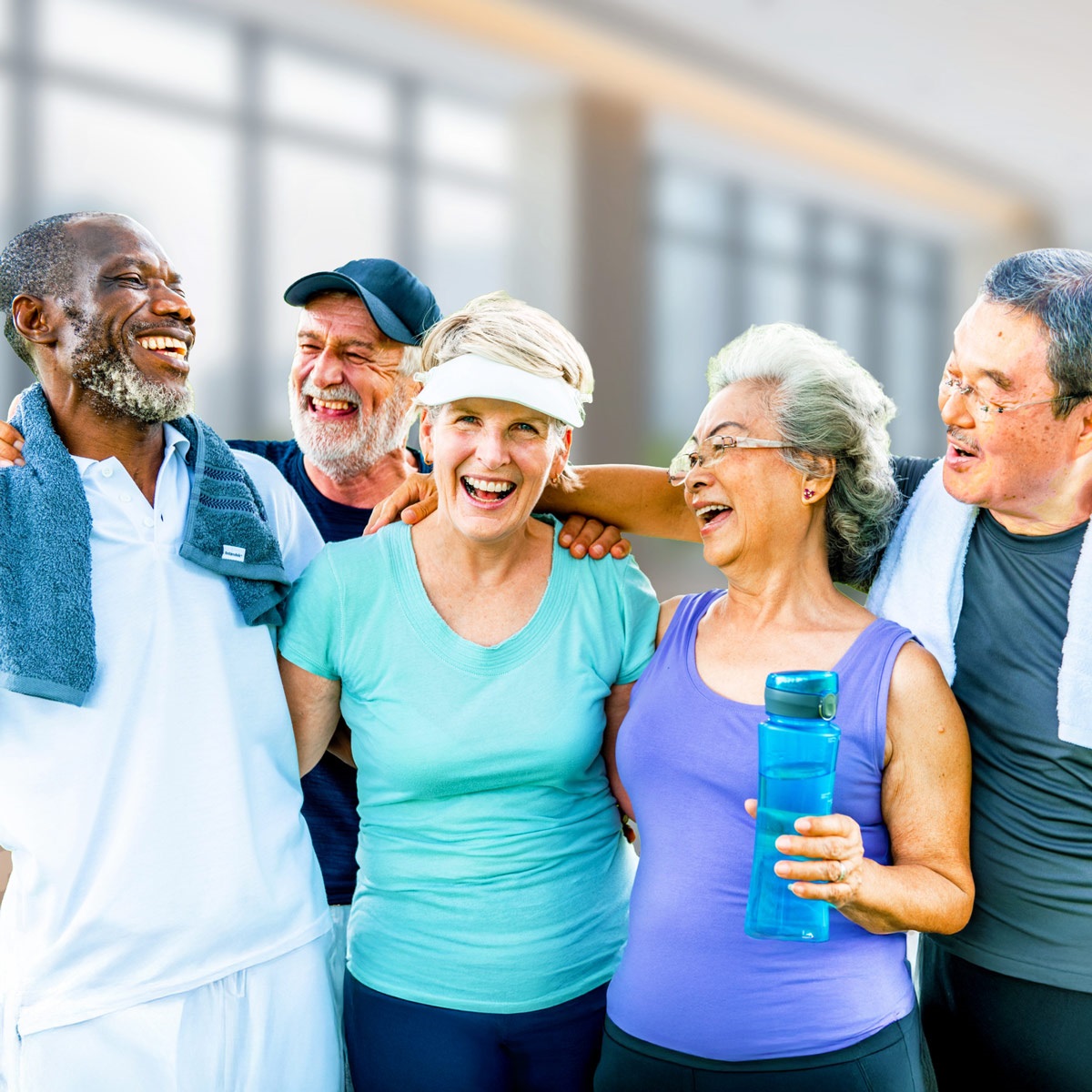 a group of older ladies and men in workout clothes embrace and our laughing.