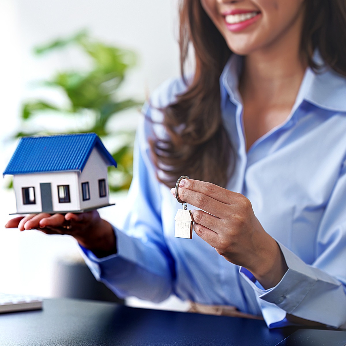 A smiling realtor, holding a model of house in her hand.