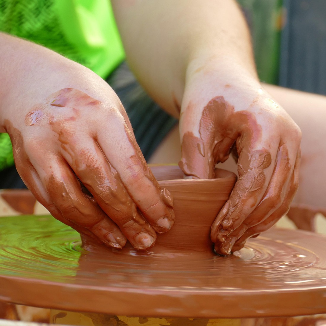 Teen creating clay dish using a pottery wheel.