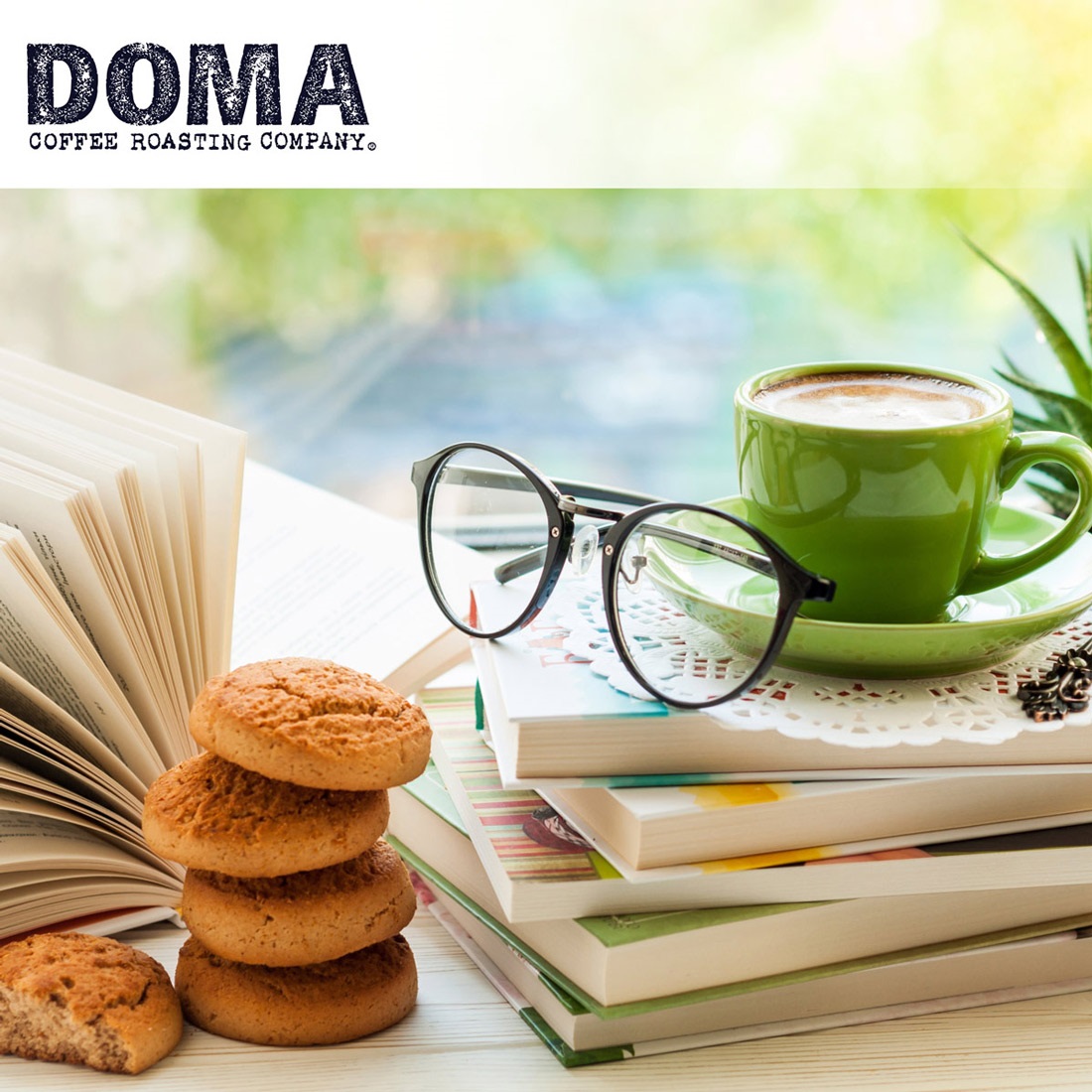 A cup of coffee on a stack of books in a coffee shop with the Doma logo