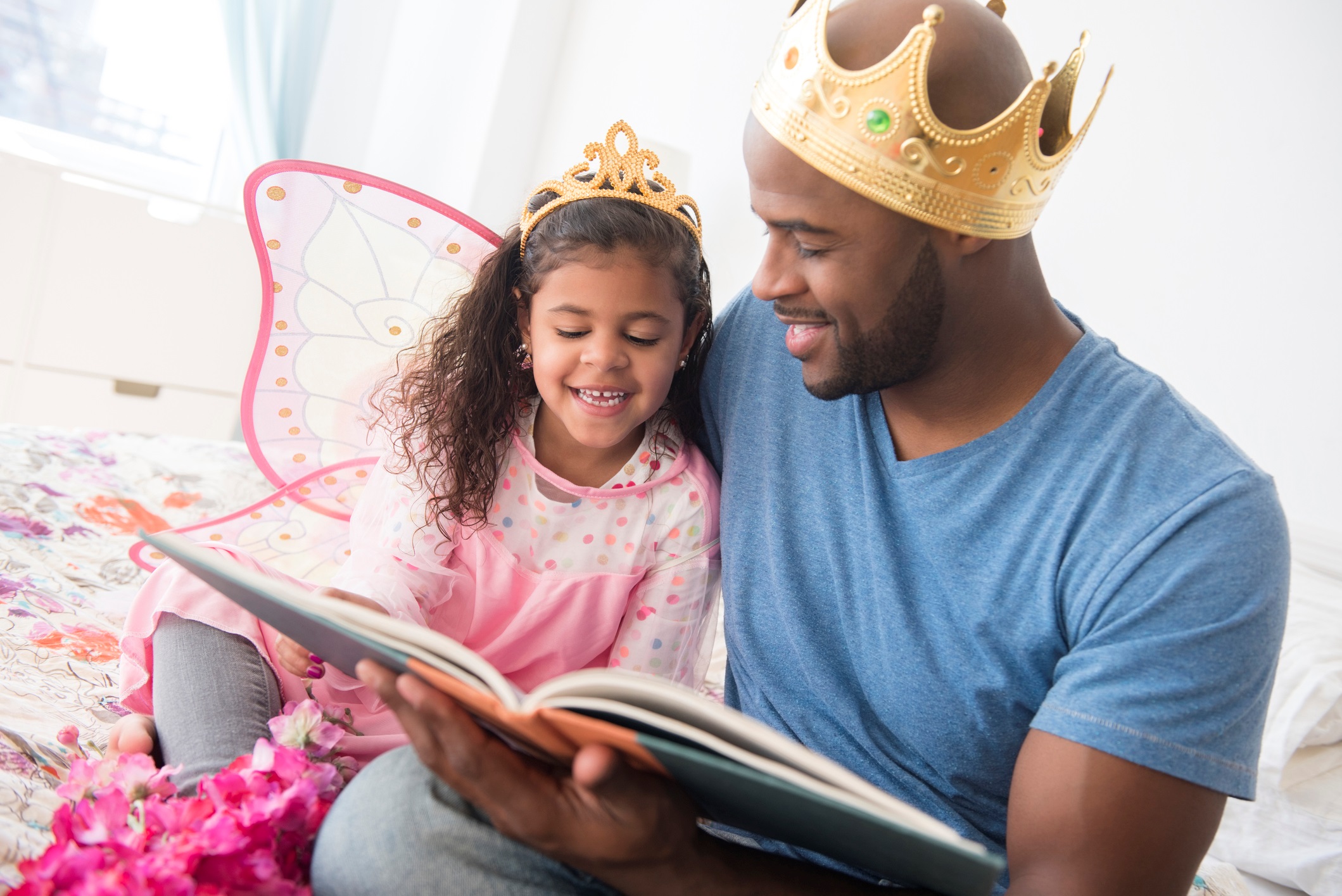 African American father wearing a crown reading with daughter