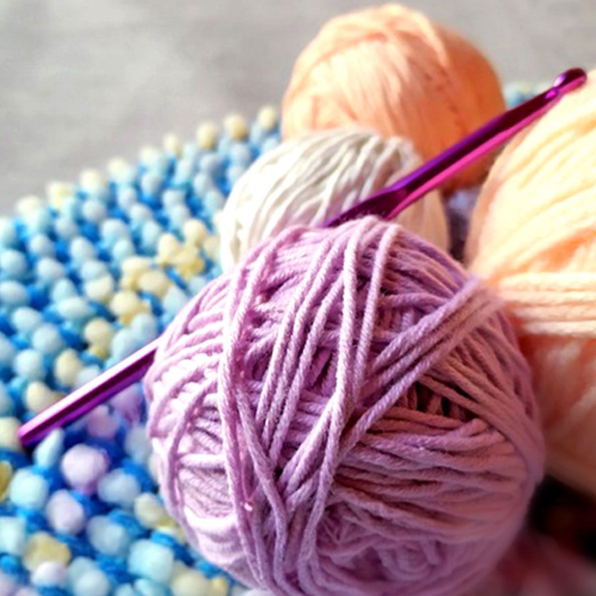 This picture shows four balls of yarn and a crochet needle resting on them.